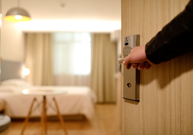 someone opening the door to a hotel room with a bed in the background